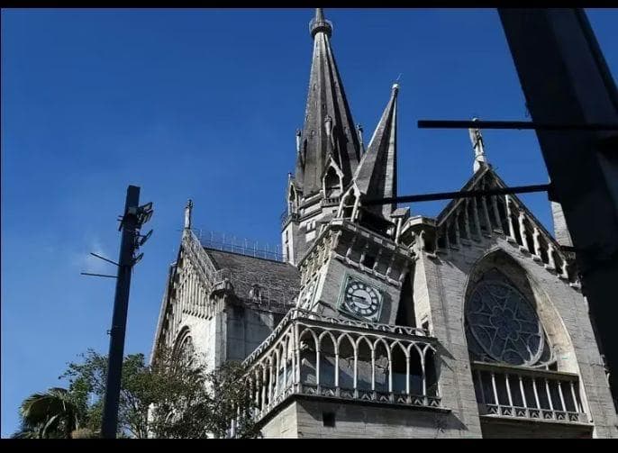 The stone spires, clock face and rose window of a Gothic cathedral against a clear sky.